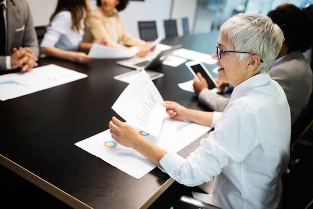 Woman sitting in a meeting with papers in her hand, smiling.